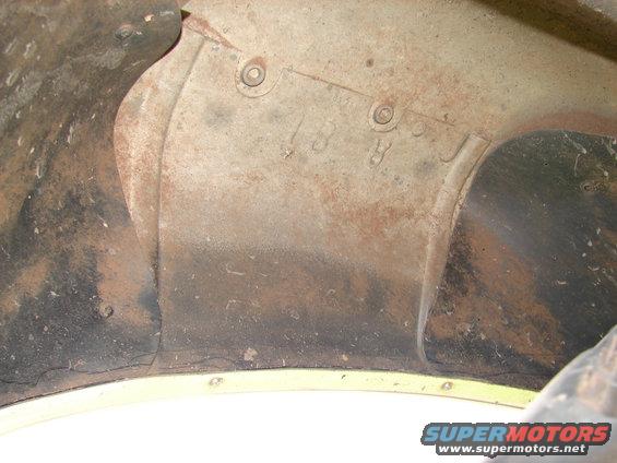 Close-up of rusty metal with numbers stamped on it, likely part of a vehicle's inner fender