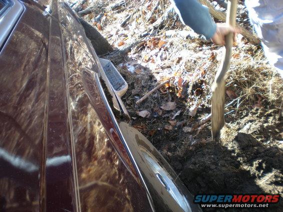 Maroon 1996 Ford Bronco side view, stuck in mud with a person digging