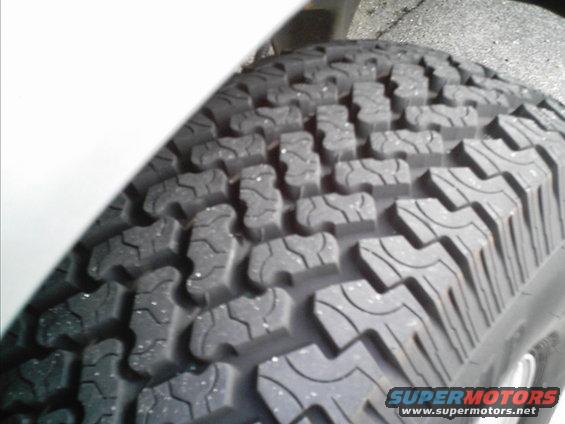 Close-up of a tire tread pattern with white specks. "SUPERMOTORS www.supermotors.net" text at bottom right