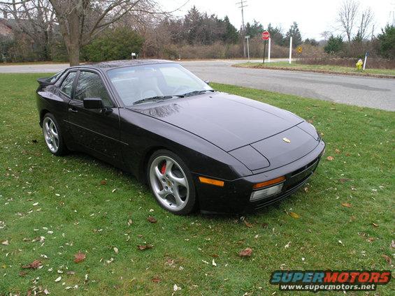 Black 1988 Porsche 944 coupe parked on grass with a road and trees in the background