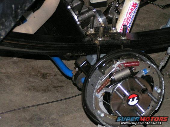 Rear drum brake assembly with shock absorber and blue hose. Supermotors.net logo visible