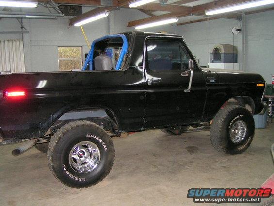 Black pickup truck with a blue roll cage inside, lifted with off-road tires. It's in a garage