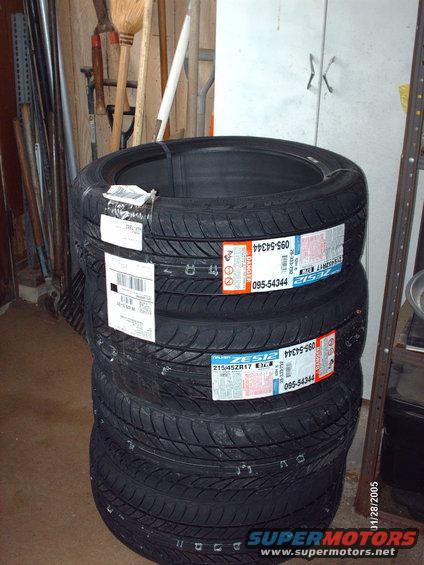Stack of four new black tires with orange and white labels, one label reads 215/45ZR17