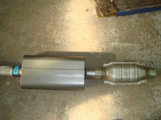 Exhaust muffler and catalytic converter on concrete floor. Muffler has "Flowmaster" text