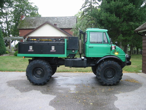 Green Unimog truck with a black toolbox bed, parked on a wet driveway