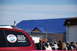 1996 Ford Bronco - A red SUV is parked in front of a building with a blue roof, with a crowd of people in the background.
