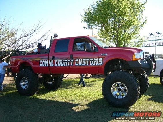 Red lifted Ford F-250 Super Duty pickup truck with "COMAL COUNTY CUSTOMS" on the side