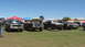1978 Ford Bronco - Several trucks and SUVs are parked on a grassy field under a clear blue sky.