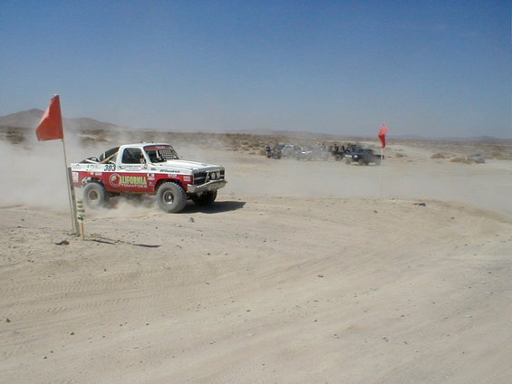 White and red off-road truck with number 303, kicking up dust on a dirt track