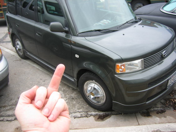 Dark green SUV, front 3/4 view, with a hand giving the middle finger