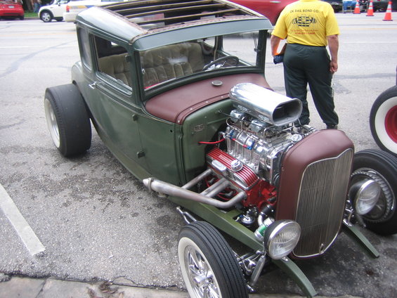 Green hot rod coupe with a large chrome blower on the V8 engine, exposed exhaust pipes, and a sunroof