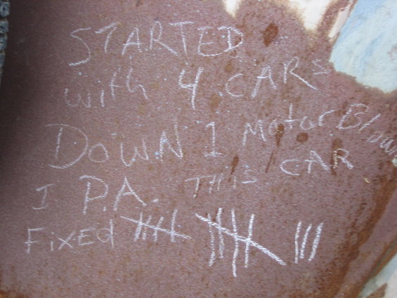chalk writing on rusty metal: 'STARTED with 4 CARS DOWN 1 motor blown I P.A. THIS CAR FIXED' with tally marks