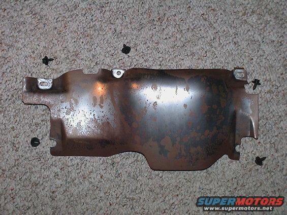 Rusty metal heat shield with four screws on a carpeted surface