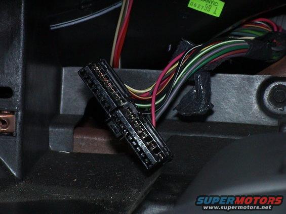 Close-up of a black multi-pin wiring harness connector with colorful wires attached, inside a vehicle