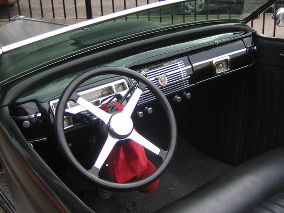1940s car interior with a black steering wheel, chrome accents, and a red hat hanging from the steering column