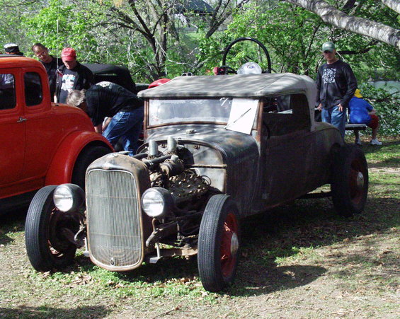 Rat rod hot rod with exposed engine and soft top. Another car is parked next to it