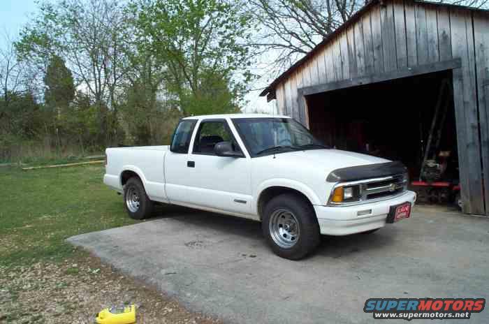 White Chevrolet S-10 pickup truck, extended cab, parked on a concrete pad in front of a wooden shed