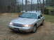 2004 Ford Crown Victoria - This sedan is parked on a dirt lot with trees and a lake in the background.