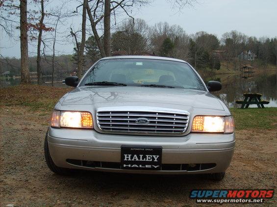 Silver 2004 Ford Crown Victoria front view with headlights on, parked outdoors near a lake