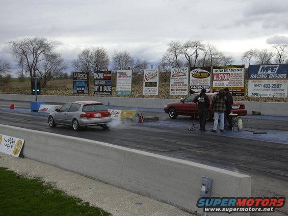 Red sedan at drag strip with people standing nearby