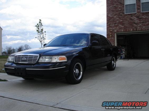 Black 2001 Ford Crown Victoria parked on a concrete driveway in front of a brick house with an open garage