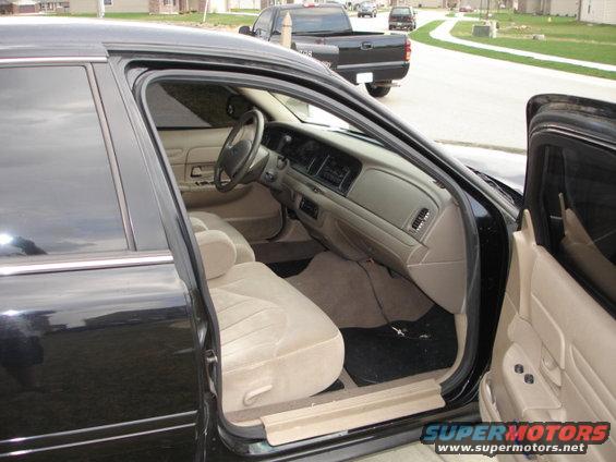 Interior of a black 2001 Ford Crown Victoria with tan seats and dashboard. A black pickup truck is visible outside