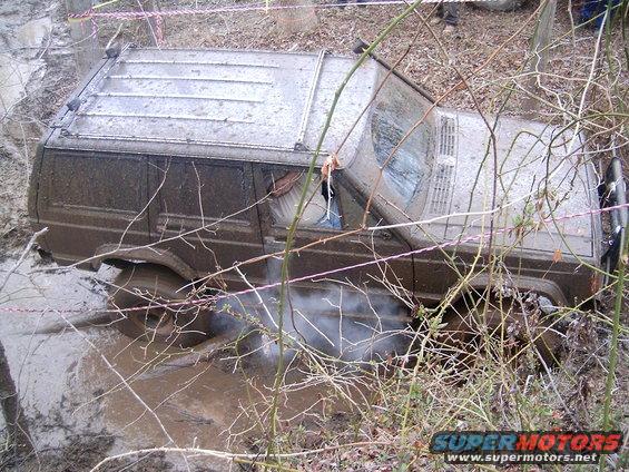 Muddy Jeep Cherokee XJ stuck in a muddy ditch with smoke coming from under the vehicle