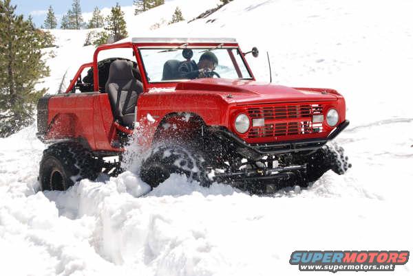 Red off-road vehicle with large tires driving through deep snow