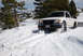 1989 Ford Bronco - A white Toyota Tacoma navigates a snowy mountain road, kicking up snow as it drives.