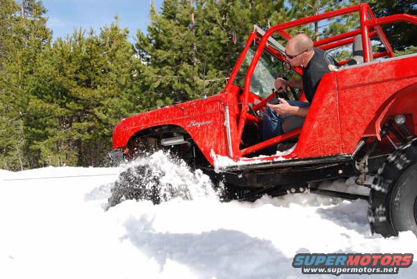 Red off-road vehicle with roll cage driving through deep snow, driver visible