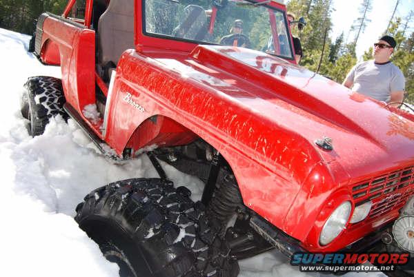Red Ford Bronco with large tires stuck in snow, front quarter view