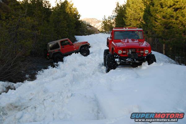 Red 1966 Ford Bronco driving through snow with another vehicle behind