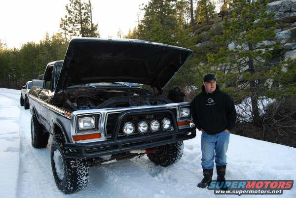 Man standing next to a 1979 Ford F-Series truck with hood open in the snow. Another truck is behind it