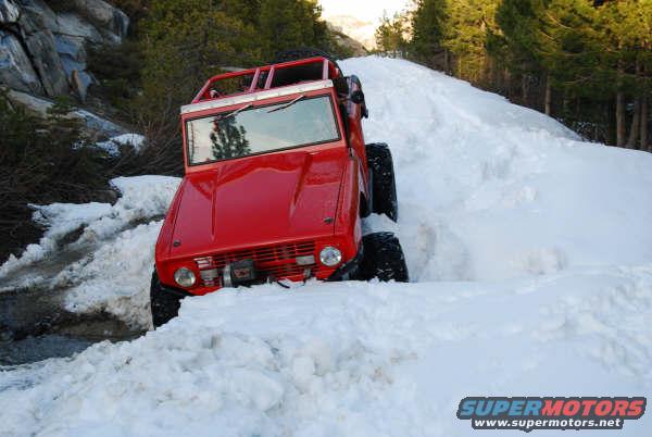 Red 1978 Ford Bronco driving through deep snow on a mountain road