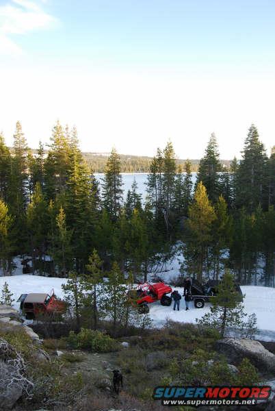 Red ATV and a dark off-road vehicle with a trailer in snow, with a dog in the foreground