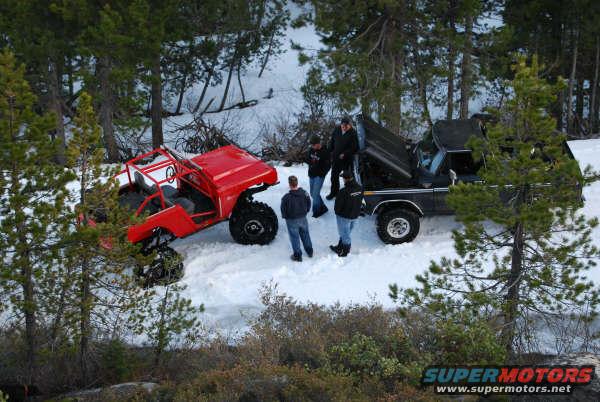 Red off-road vehicle and black pickup truck in snow with people
