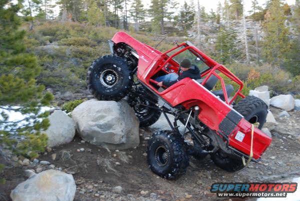 Red off-road vehicle with large tires climbing over rocks on a dirt trail