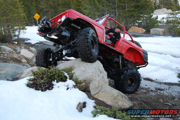 Red off-road vehicle with large tires climbing over rocks and snow