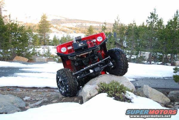Red 1989 Ford Bronco off-roading over rocks in a snowy landscape