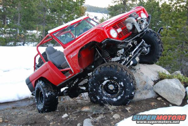 1989 Ford Bronco modified for off-roading, with large tires and roll cage, on rocky terrain with snow