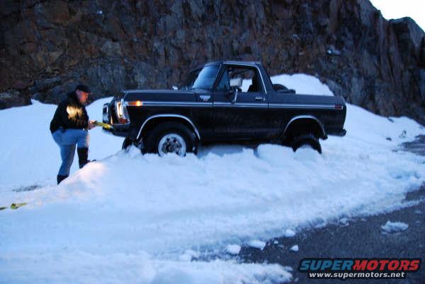 Man trying to free a black Ford Bronco stuck in deep snow
