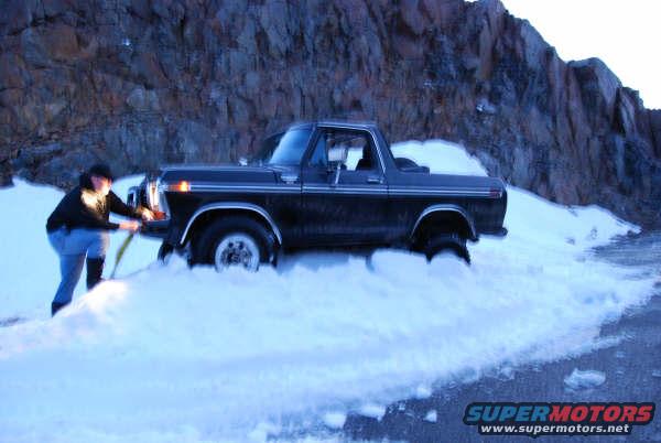 Black Ford Bronco stuck in deep snow, driver shoveling snow from front wheel