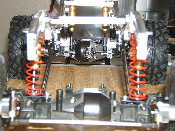 Close-up of an RC crawler's rear suspension with red springs and chrome shocks