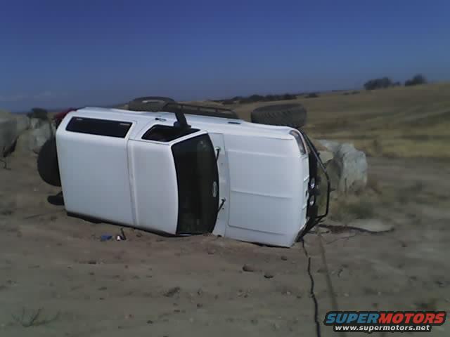 1995 Ford Bronco on its side in a dirt field with rocks and dry grass