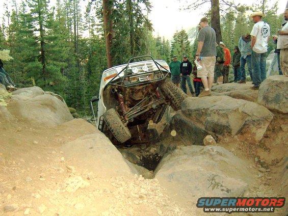 White off-road SUV tilted on its side, stuck between large rocks on a dirt trail