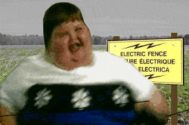 guy in a field next to an electric fence sign