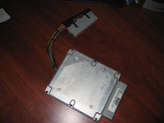 Ford engine control module with wiring harness attached, sitting on a wooden surface