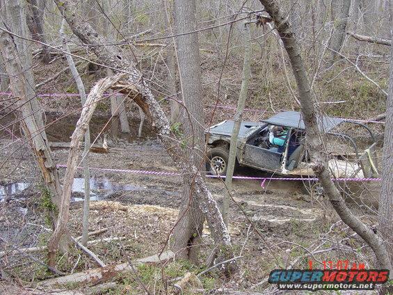 Off-road vehicle with open doors stuck in muddy terrain surrounded by trees