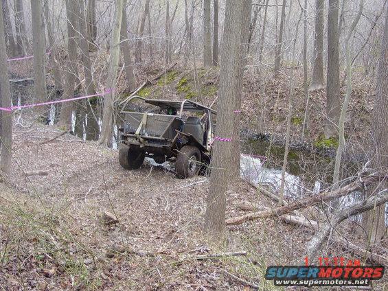 Off-road vehicle with no top or doors, parked on a wooded trail near a stream