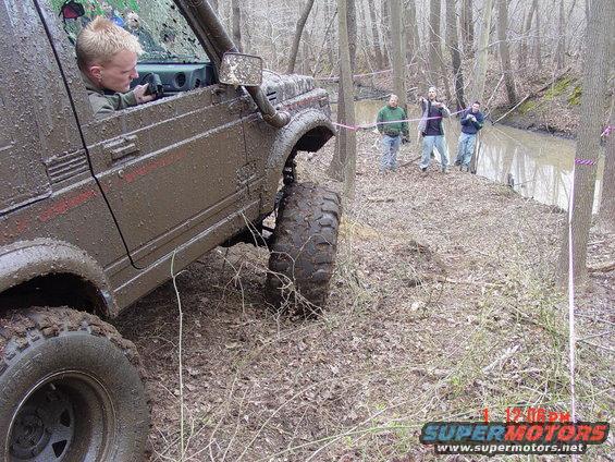 Mud-covered Suzuki Samurai off-roading with a driver inside, tires deep in mud